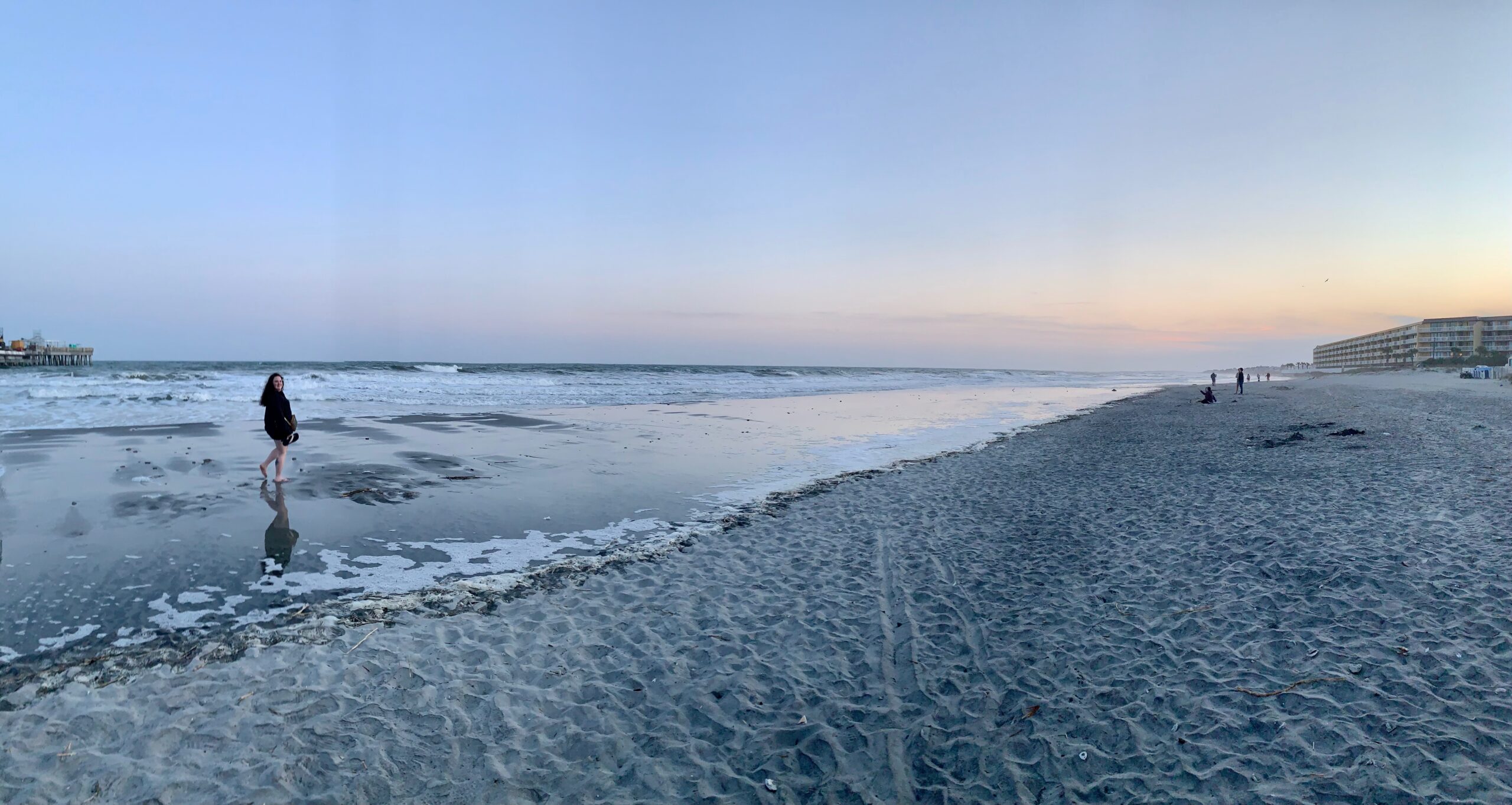 A woman stands to the left of an expansive photo of a South Carolina beach during sunset