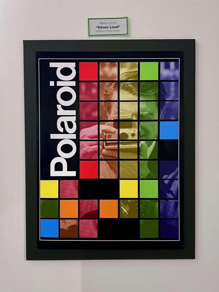 A poster of colorful grid squares in iconic Polaroid colors, red, orange, yellow, green, and blue. The squares mask a black and white photo of Edwin Land aiming a vintage Polaroid camera at the viewer. The black background is contrasted heavily with a bright white Polaroid text logo, turned 90º to the right.