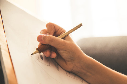 A black and white photo of a right hand drawing with a pencil on a piece of paper.