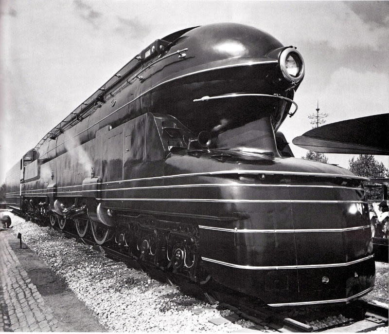 A black and white photograph of Loewy's streamlined locomotive design. A large rounded train comes into closer perspective from the left side of the image.